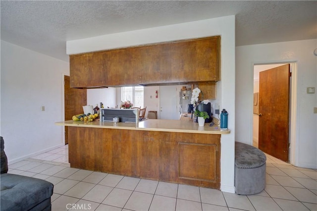 2120 Ocean St, Oceano, CA 93445 - kitchen featuring brown cabinets, a peninsula, light countertops, light tile patterned flooring, and a textured ceiling
