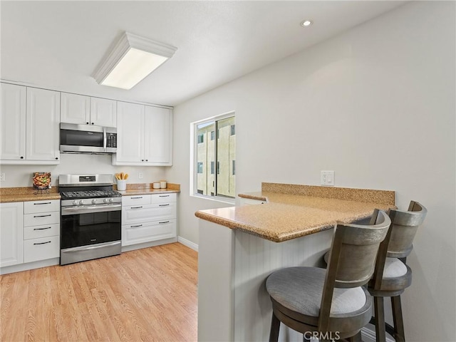 9531 Via Ricardo, Sun Valley, CA 91504 - kitchen with stainless steel appliances, a kitchen bar, white cabinetry, light wood-type flooring, and a peninsula