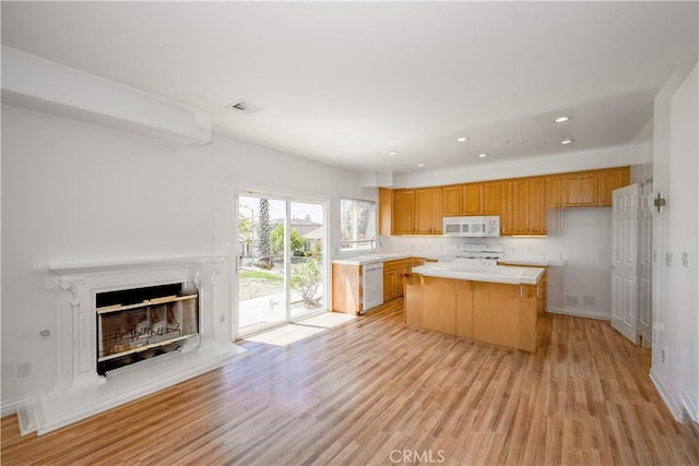 13056 Hagar St, Sylmar, CA 91342 - kitchen featuring white appliances, light countertops, light wood-type flooring, a center island, and a fireplace with raised hearth