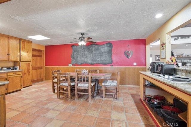 60810 Sunrise Rd, Whitewater, CA 92282 - dining room featuring a ceiling fan, a wainscoted wall, wooden walls, a textured ceiling, and stone tile flooring