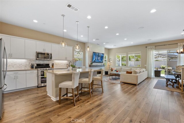 28816 Sedge Ln, Saugus, CA 91350 - kitchen with appliances with stainless steel finishes, an island with sink, white cabinetry, light wood finished floors, and a breakfast bar