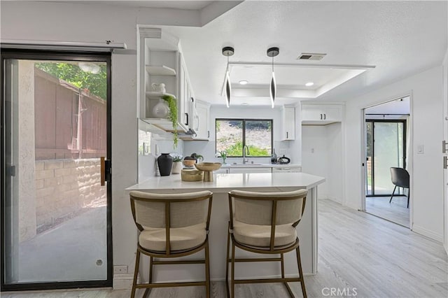 15775 Caminito Atico, San Diego, CA 92128 - kitchen with a peninsula, white cabinetry, light countertops, open shelves, and light wood-style floors