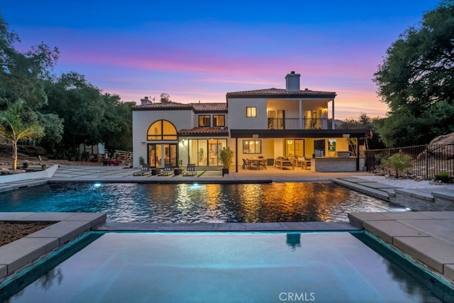 176 Saddlebow Rd, Bell Canyon, CA 91307 - back of house at dusk featuring a chimney, a balcony, stucco siding, a patio, and a tiled roof