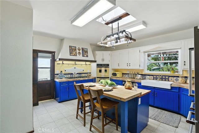 1215 S Patton Ave, San Pedro, CA 90731 - kitchen with butcher block counters, blue cabinets, multiple ovens, light tile patterned floors, and premium range hood
