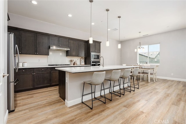 2070 Solig Ave, Kingsburg, CA 93631 - kitchen featuring under cabinet range hood, stainless steel appliances, light wood-type flooring, a kitchen breakfast bar, and recessed lighting