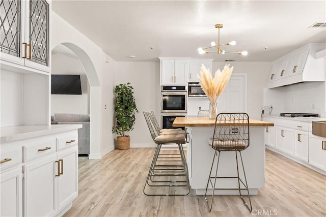 35356 Sierra Vista Dr, Agua Dulce, CA 91390 - kitchen with stainless steel double oven, butcher block counters, a kitchen bar, white cabinetry, and arched walkways
