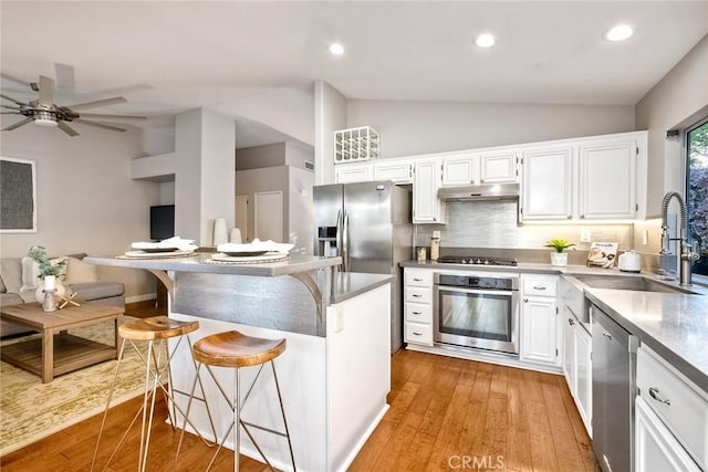 591 Shadow Tree Dr, Oceanside, CA 92058 - kitchen featuring appliances with stainless steel finishes, lofted ceiling, under cabinet range hood, white cabinetry, and a breakfast bar
