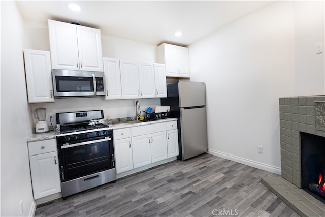 425 W 17th St, San Bernardino, CA 92405 - kitchen featuring appliances with stainless steel finishes, light wood-style flooring, white cabinets, a fireplace, and recessed lighting