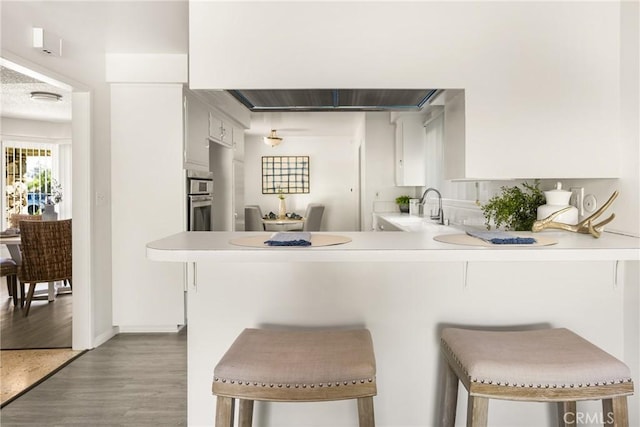 557 S Gardner Dr, Orange, CA 92866 - kitchen with a peninsula, light wood finished floors, light countertops, a breakfast bar area, and white cabinetry