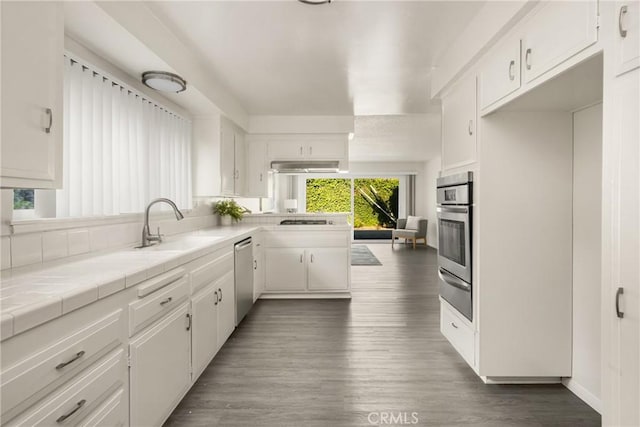 557 S Gardner Dr, Orange, CA 92866 - kitchen featuring stainless steel appliances, white cabinets, wood finished floors, tile counters, and a peninsula