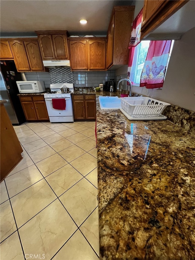 2932 Prospect Ave, Riverside, CA 92507 - kitchen with white appliances, under cabinet range hood, decorative backsplash, dark stone counters, and brown cabinets