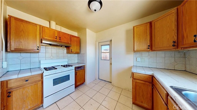 21845 Fox Ave, Apple Valley, CA 92307 - kitchen with white range with gas stovetop, under cabinet range hood, tile counters, tasteful backsplash, and brown cabinets