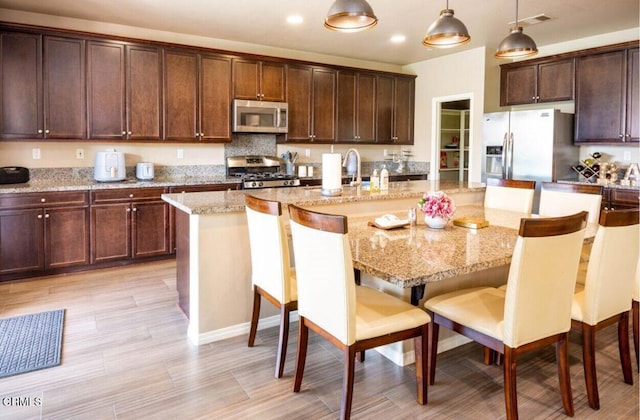 84319 Cigno Ct, Indio, CA 92203 - kitchen featuring stainless steel appliances, an island with sink, a kitchen bar, pendant lighting, and light stone counters