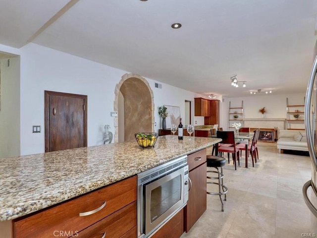 25152 Mammoth Cir, Lake Forest, CA 92630 - kitchen featuring stainless steel microwave, brown cabinets, light stone countertops, and arched walkways
