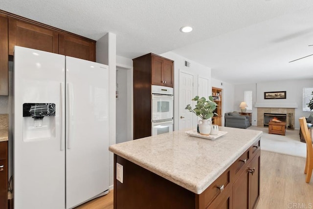 4356 Point Reyes Ct, Carlsbad, CA 92010 - kitchen featuring white appliances, light wood-style floors, a tile fireplace, a center island, and light countertops
