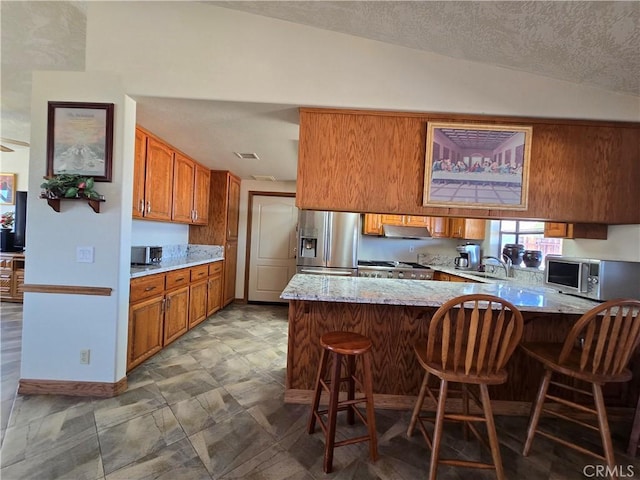 7050 Ivanpah Ave Unit 29, Palms, CA 92277 - kitchen featuring appliances with stainless steel finishes, vaulted ceiling, a peninsula, brown cabinets, and a kitchen breakfast bar