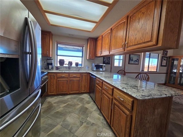 7050 Ivanpah Ave Unit 29, Palms, CA 92277 - kitchen featuring stainless steel appliances, a peninsula, brown cabinets, and light stone countertops