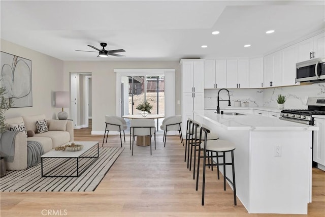 7364 Layton St, Rancho Cucamonga, CA 91730 - kitchen featuring stainless steel appliances, white cabinetry, a breakfast bar area, light wood-style floors, and a center island with sink
