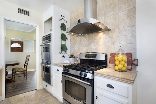 829 N Foxdale Ave, West Covina, CA 91790 - kitchen featuring wall chimney range hood, appliances with stainless steel finishes, white cabinets, decorative backsplash, and light tile patterned floors