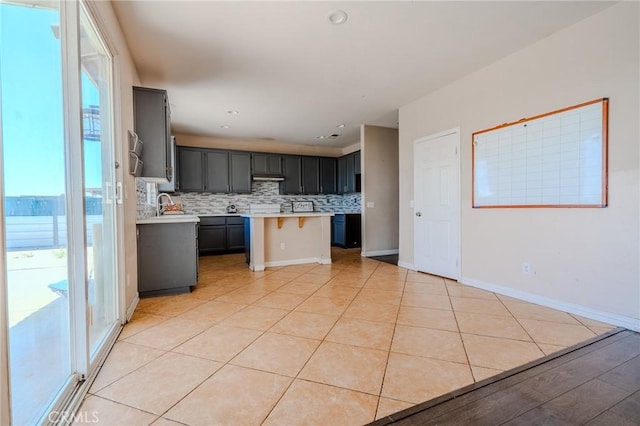 11818 Forest Park Ln, Victorville, CA 92392 - kitchen featuring light countertops, tasteful backsplash, a kitchen breakfast bar, light tile patterned floors, and under cabinet range hood