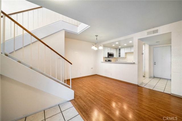 12277 Foster Rd, Norwalk, CA 90650 - unfurnished living room with stairs, light wood-style flooring, a chandelier, a skylight, and recessed lighting