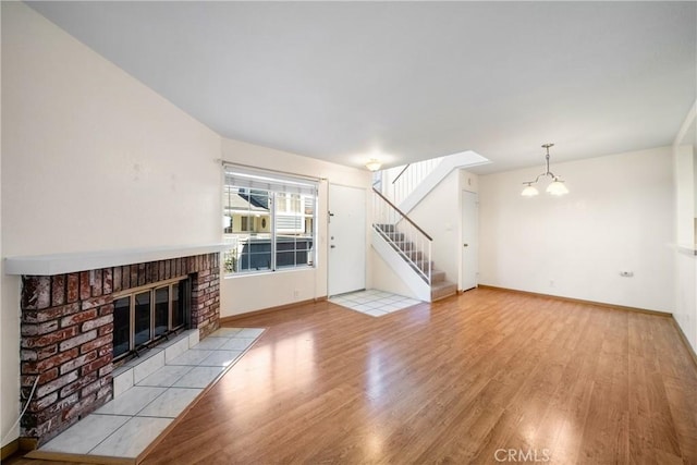 12277 Foster Rd, Norwalk, CA 90650 - unfurnished living room with light wood-style flooring, a chandelier, a brick fireplace, and stairs