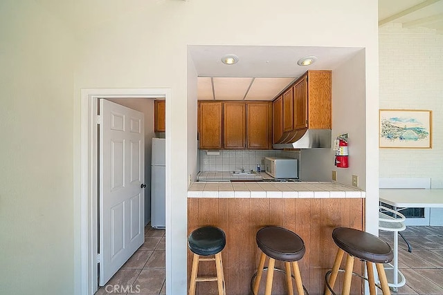 2209 W 25th St Unit 7, San Pedro, CA 90732 - kitchen featuring white appliances, tile countertops, brown cabinetry, a kitchen breakfast bar, and decorative backsplash