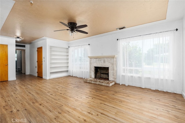 4491 N Dewitt Ave, Fresno, CA 93727 - unfurnished living room with built in features, a ceiling fan, wood finished floors, a fireplace with raised hearth, and a textured ceiling