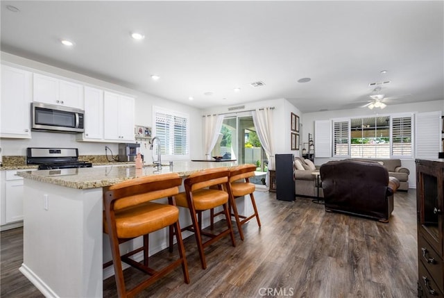 30159 Honor Ct, Menifee, CA 92584 - kitchen with stainless steel appliances, open floor plan, dark wood-style flooring, a kitchen island with sink, and light stone counters