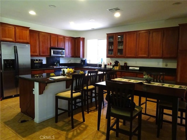 43890 Moccasin Pl, Lancaster, CA 93536 - kitchen featuring stainless steel appliances, light tile patterned floors, dark brown cabinets, dark countertops, and a breakfast bar area