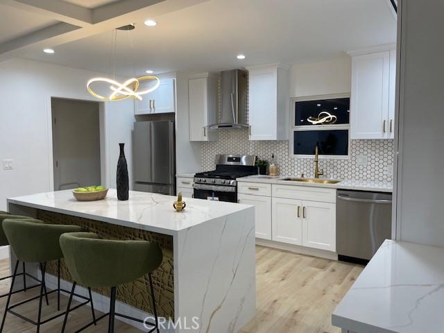 20406 Londelius St, Winnetka, CA 91306 - kitchen with appliances with stainless steel finishes, wall chimney range hood, light wood-type flooring, decorative backsplash, and a kitchen island