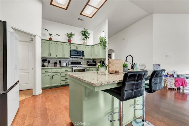 695 Crescent Ln, Lemoore, CA 93245 - kitchen with green cabinets, appliances with stainless steel finishes, a peninsula, a breakfast bar, and decorative backsplash