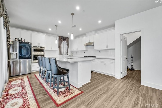 16614 Trailblazer Ave, Chino, CA 91708 - kitchen with stainless steel appliances, under cabinet range hood, light countertops, light wood-type flooring, and a center island with sink