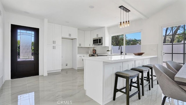 23231 Cheswald Dr, Laguna Niguel, CA 92677 - kitchen featuring stainless steel microwave, light marble finish flooring, a breakfast bar, and white cabinetry