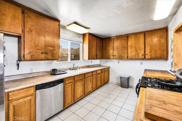 5177 Avenida Del Sol, Joshua Tree, CA 92252 - kitchen featuring stainless steel dishwasher, black gas range oven, light tile patterned floors, light countertops, and brown cabinets