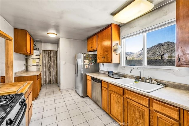 5177 Avenida Del Sol, Joshua Tree, CA 92252 - kitchen featuring appliances with stainless steel finishes, light countertops, brown cabinetry, light tile patterned flooring, and secured water heater