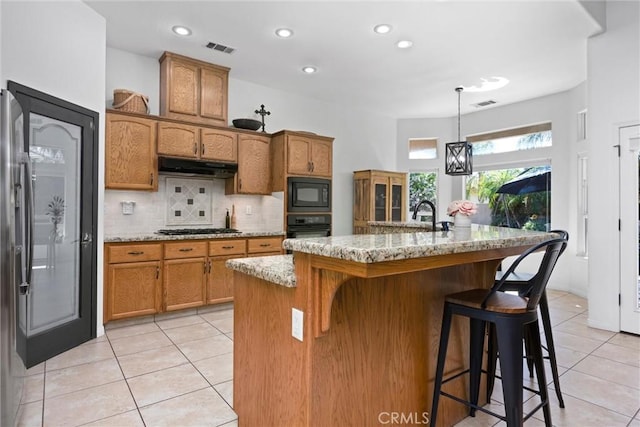 403 Stone Cross Dr, Bakersfield, CA 93312 - kitchen featuring black appliances, under cabinet range hood, light tile patterned floors, brown cabinets, and decorative backsplash