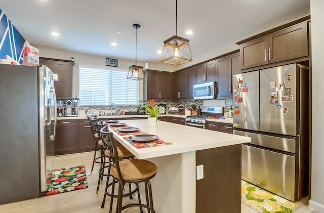 1905 Soho Ln Unit 2, Chula Vista, CA 91915 - kitchen with appliances with stainless steel finishes, dark brown cabinetry, a breakfast bar area, tasteful backsplash, and light countertops
