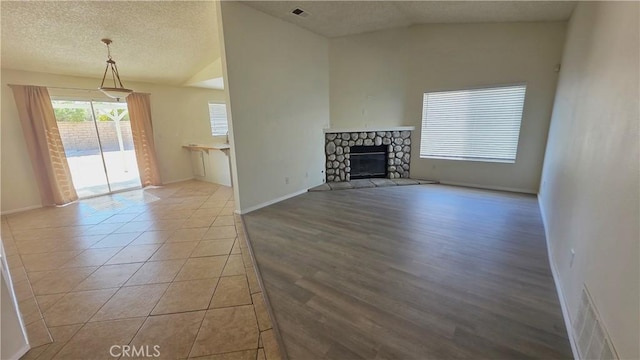37432 Whitehall Ln, Palmdale, CA 93550 - unfurnished living room with lofted ceiling, a stone fireplace, a textured ceiling, and tile patterned flooring