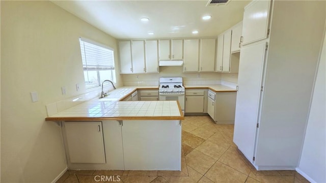 37432 Whitehall Ln, Palmdale, CA 93550 - kitchen with white gas range oven, a peninsula, tile counters, under cabinet range hood, and recessed lighting