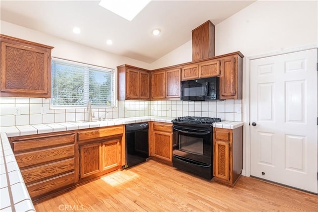 5335 Play Doe Ln, Paso Robles, CA 93446 - kitchen with black appliances, tile counters, vaulted ceiling, light wood-style flooring, and tasteful backsplash