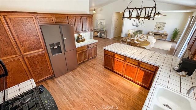 5335 Play Doe Ln, Paso Robles, CA 93446 - kitchen with stainless steel fridge with ice dispenser, tile counters, brown cabinets, light wood-style flooring, and vaulted ceiling