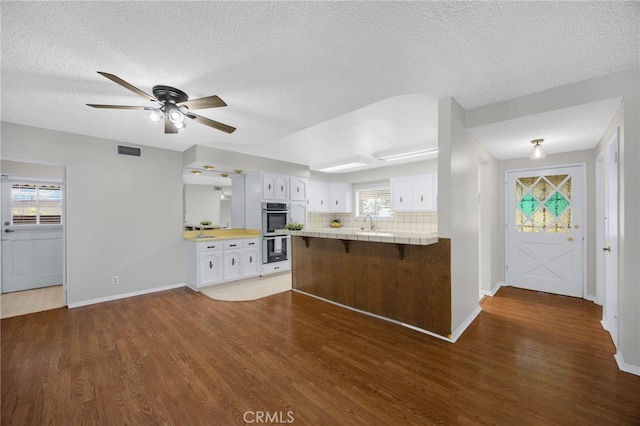 10802 Jordan Rd, Whittier, CA 90603 - kitchen featuring stainless steel double oven, dark wood-style floors, white cabinetry, a textured ceiling, and a peninsula