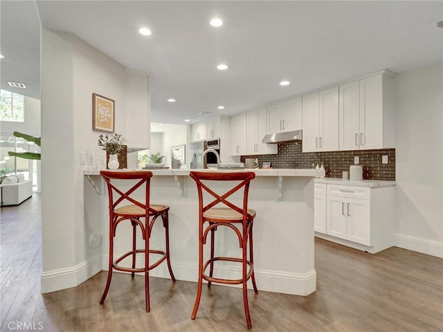 23034 Park Este, Calabasas, CA 91302 - kitchen with under cabinet range hood, a kitchen breakfast bar, wood finished floors, white cabinetry, and a peninsula