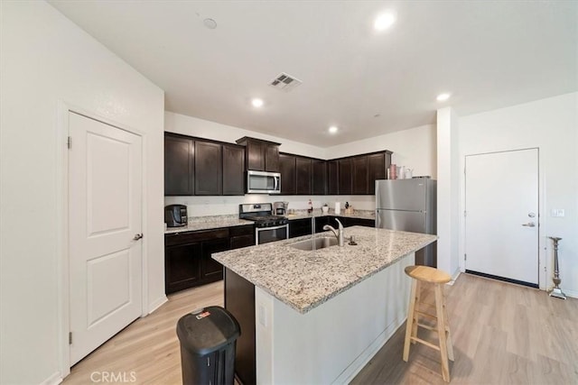 16814 Desert Star St, Victorville, CA 92394 - kitchen featuring appliances with stainless steel finishes, light wood finished floors, light stone countertops, a kitchen island with sink, and recessed lighting