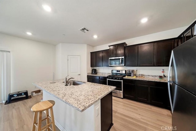 16814 Desert Star St, Victorville, CA 92394 - kitchen with stainless steel appliances, light wood finished floors, light stone countertops, a breakfast bar, and a kitchen island with sink