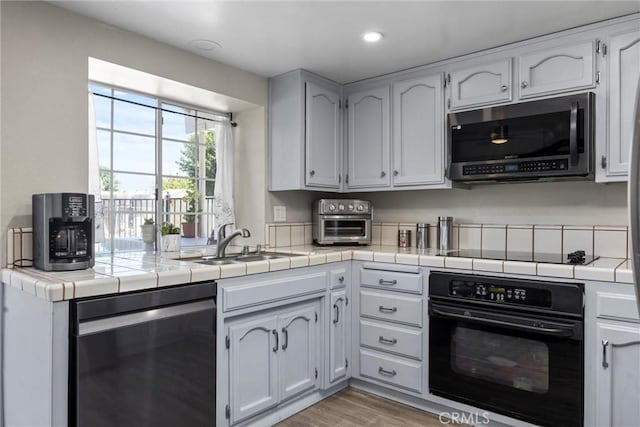 3108 Holbrook St, Bakersfield, CA 93312 - kitchen with black appliances, tile counters, light wood finished floors, recessed lighting, and white cabinetry
