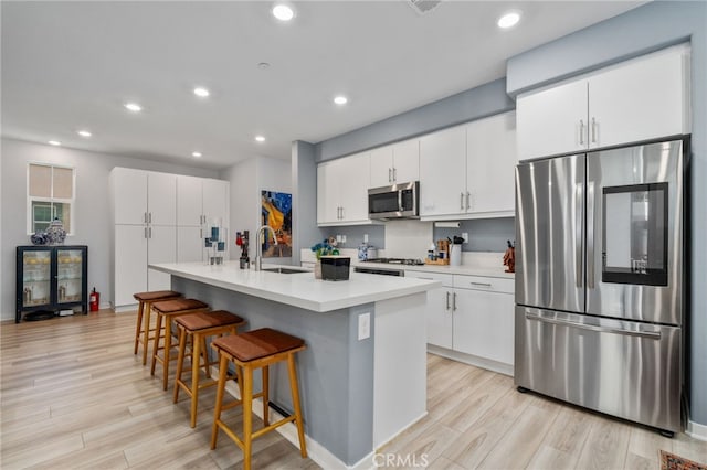 8234 Traveller St, Chino, CA 91710 - kitchen featuring appliances with stainless steel finishes, a breakfast bar, light wood finished floors, a kitchen island with sink, and white cabinetry