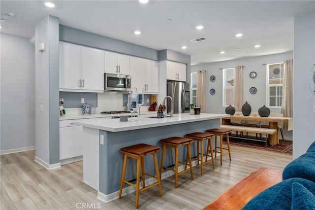 8234 Traveller St, Chino, CA 91710 - kitchen with stainless steel appliances, light wood-style flooring, a breakfast bar area, a kitchen island with sink, and white cabinetry