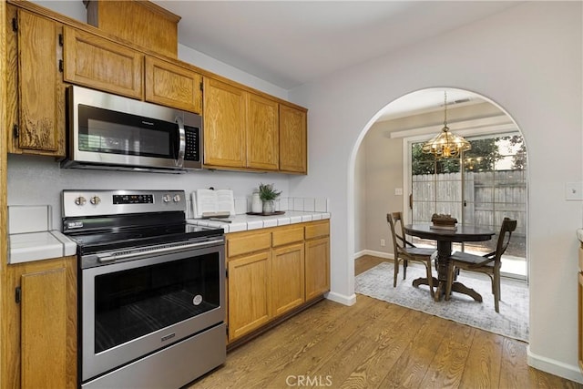 2081 Marilyn Dr, Chico, CA 95928 - kitchen featuring appliances with stainless steel finishes, arched walkways, a chandelier, wood finished floors, and tile counters